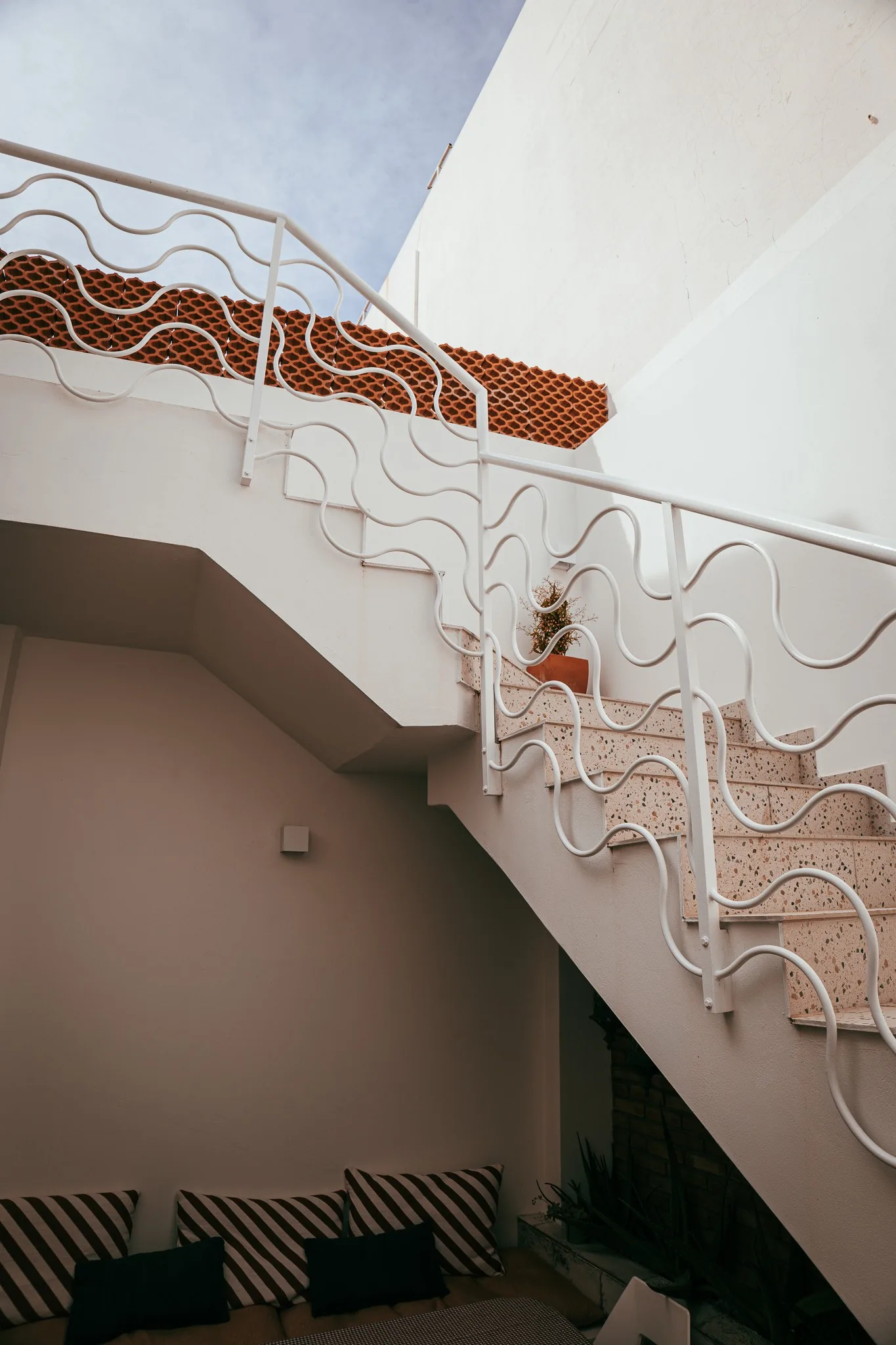 Escalier exterieur blanc a la rambarde ondulee, typique d'une maison mediterraneenne a Fuseta dans l'Algarve, avec un coin salon en contrebas.